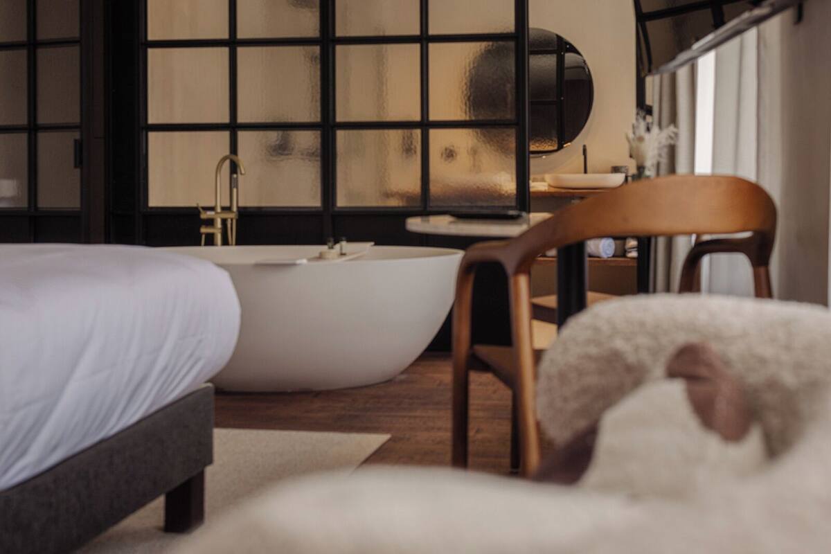 Une chambre à coucher moderne avec une grande baignoire, une chaise en bois et un lit.