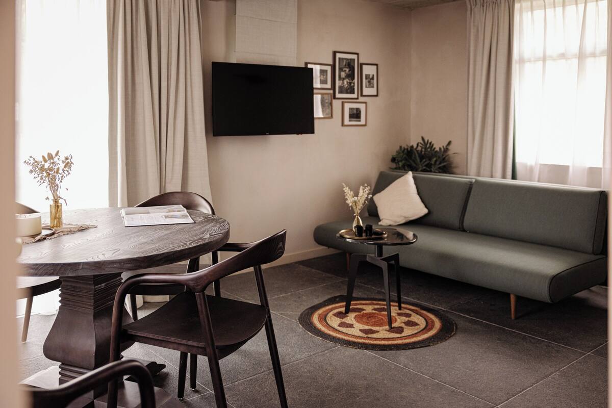 Un salon avec une table ronde, deux chaises, un canapé, un téléviseur à écran plat et des tableaux encadrés accrochés au mur.