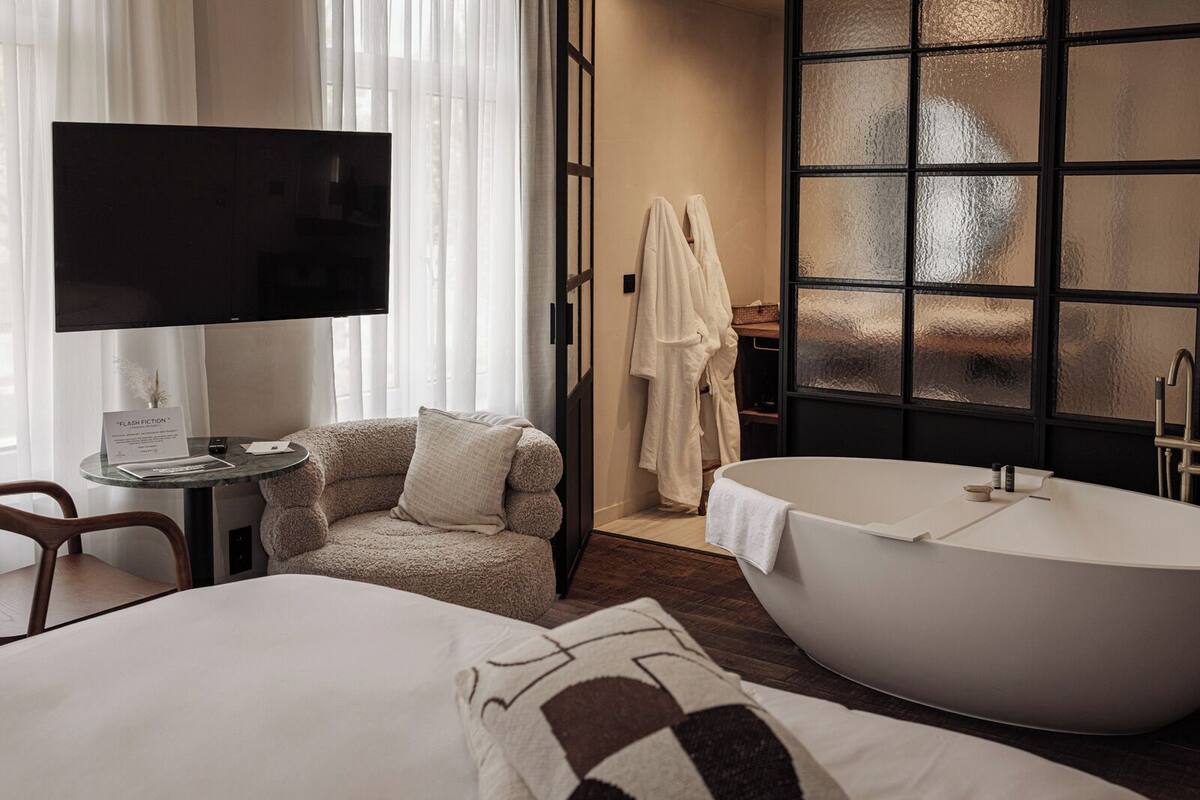 Une chambre d’hôtel avec une grande baignoire, un téléviseur, un fauteuil confortable et un bureau sur lequel est posé un panneau.