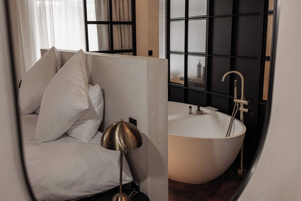 Une salle de bain moderne avec une baignoire sur pieds, une grande fenêtre aux montures noires et un canapé blanc agrémenté de coussins.