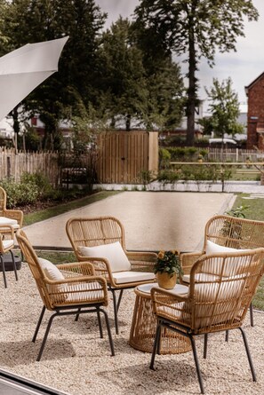 Un espace extérieur aménagé avec des chaises en osier et une table, entouré de gravier et de verdure.