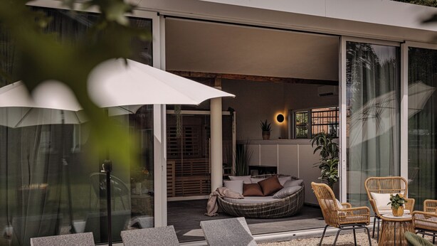 Un espacio exterior moderno con sillones de relax, un sofá de mimbre y una mesa con una planta.