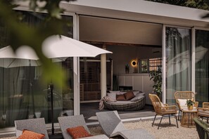 Un espacio exterior moderno con sillones de relax, un sofá de mimbre y una mesa con una planta.