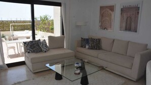 A living room with a glass coffee table, beige sofas, and a view of a balcony with outdoor furniture. - Luxury 3bedrooms apartment in Gammarth Touristique with Pool 3 Mnts beach access (Gammarth)