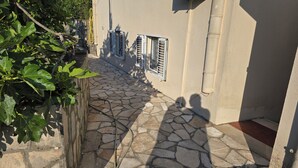 Ein gepflasterter Weg führt zu einem Gebäude mit Fensterläden und einem Schlauch an der Wand.