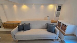 Ein modernes Wohnzimmer mit einem hellen Sofa, zwei Kissen, einer Holzbank und einem kleinen Tisch mit Körben.