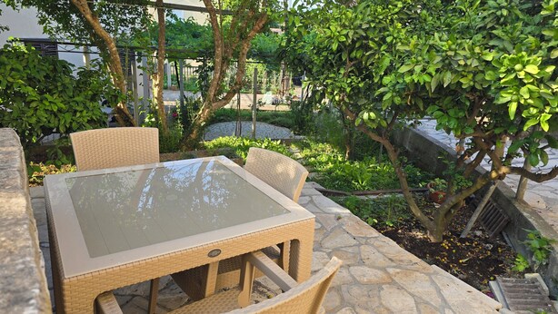 Eine Gartenpatio mit einem Tisch aus Glas und Korbstühlen, umgeben von üppiger Bepflanzung und einem Steinweg.