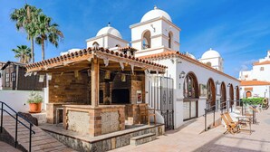 Un patio con zona de barbacoa, escalones que conducen a un edificio con torres abovedadas y palmeras.