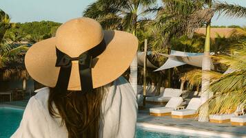 A person with a large sun hat overlooking a pool area with lounge chairs and palm trees.