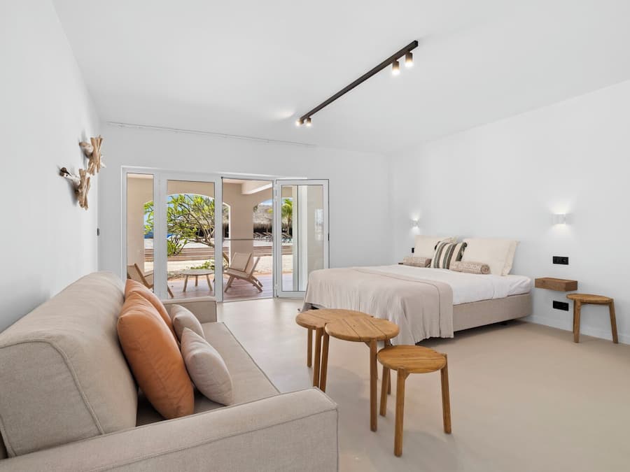 A modern hotel room with a sofa, a bed, a small table, and a view of the beach through large sliding doors.