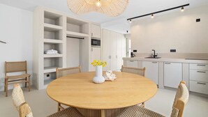 A modern kitchen with white cabinets, a round wooden table, wicker chairs, and a unique woven light fixture. - Sorobon Bay Hotel (Kralendijk)