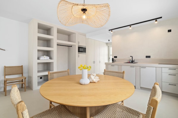 A modern kitchen with white cabinets, a round wooden table, wicker chairs, and a unique woven light fixture. - Sorobon Bay Hotel (Kralendijk)