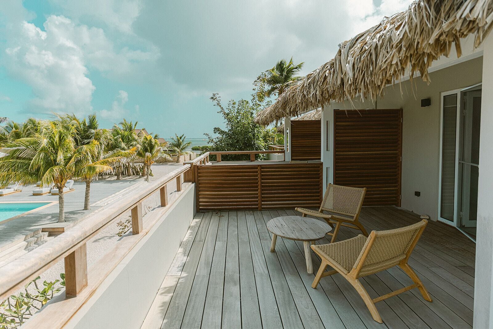 A wooden deck with a thatched roof, two wicker chairs, a pool, and a view of the ocean.