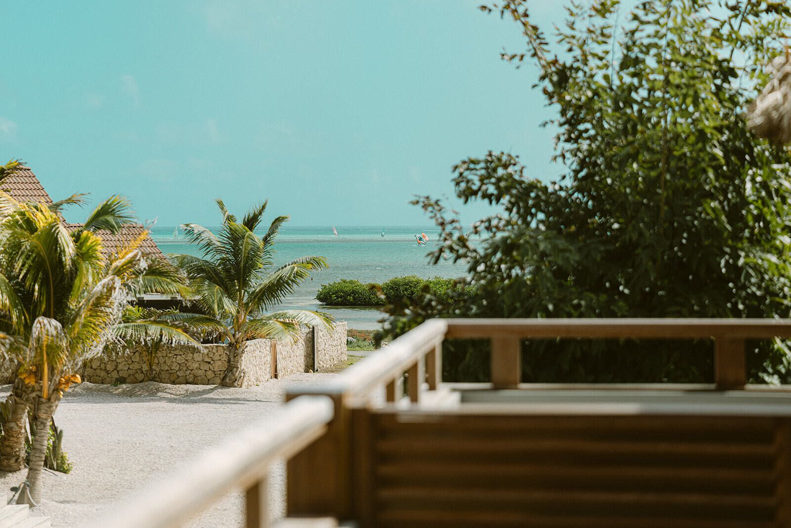 A beach view with palm trees, a wooden deck, and a stone wall.