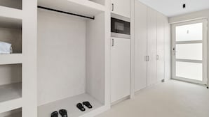 A modern, minimalist walk-in closet with built-in shelving, a shoe rack, and a microwave. - Sorobon Bay Hotel (Kralendijk)