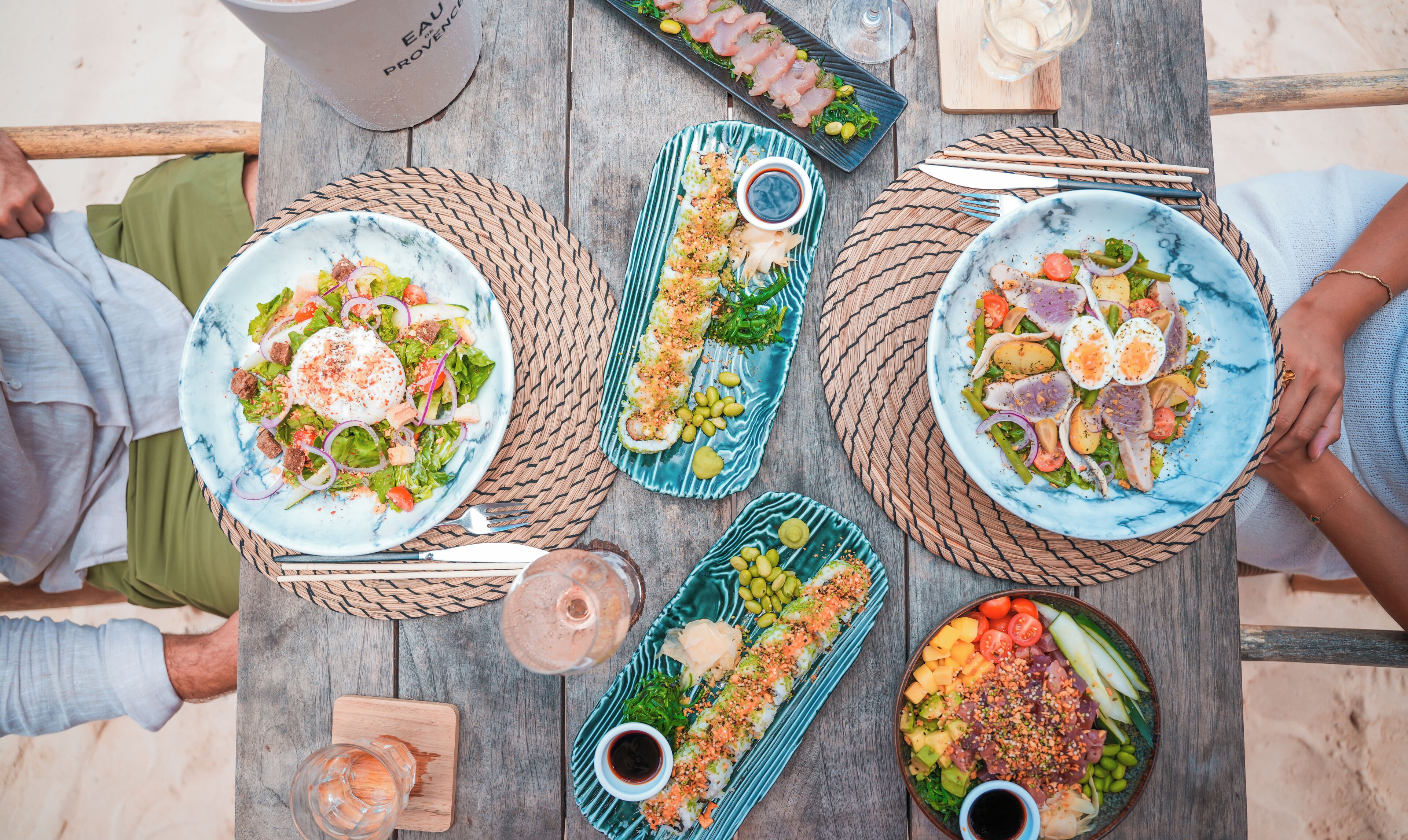 A table with various dishes, including salads and sushi, and a glass of wine.
