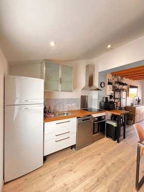 A modern kitchen with a refrigerator, dishwasher, wooden countertop, and a dining area with a chair.