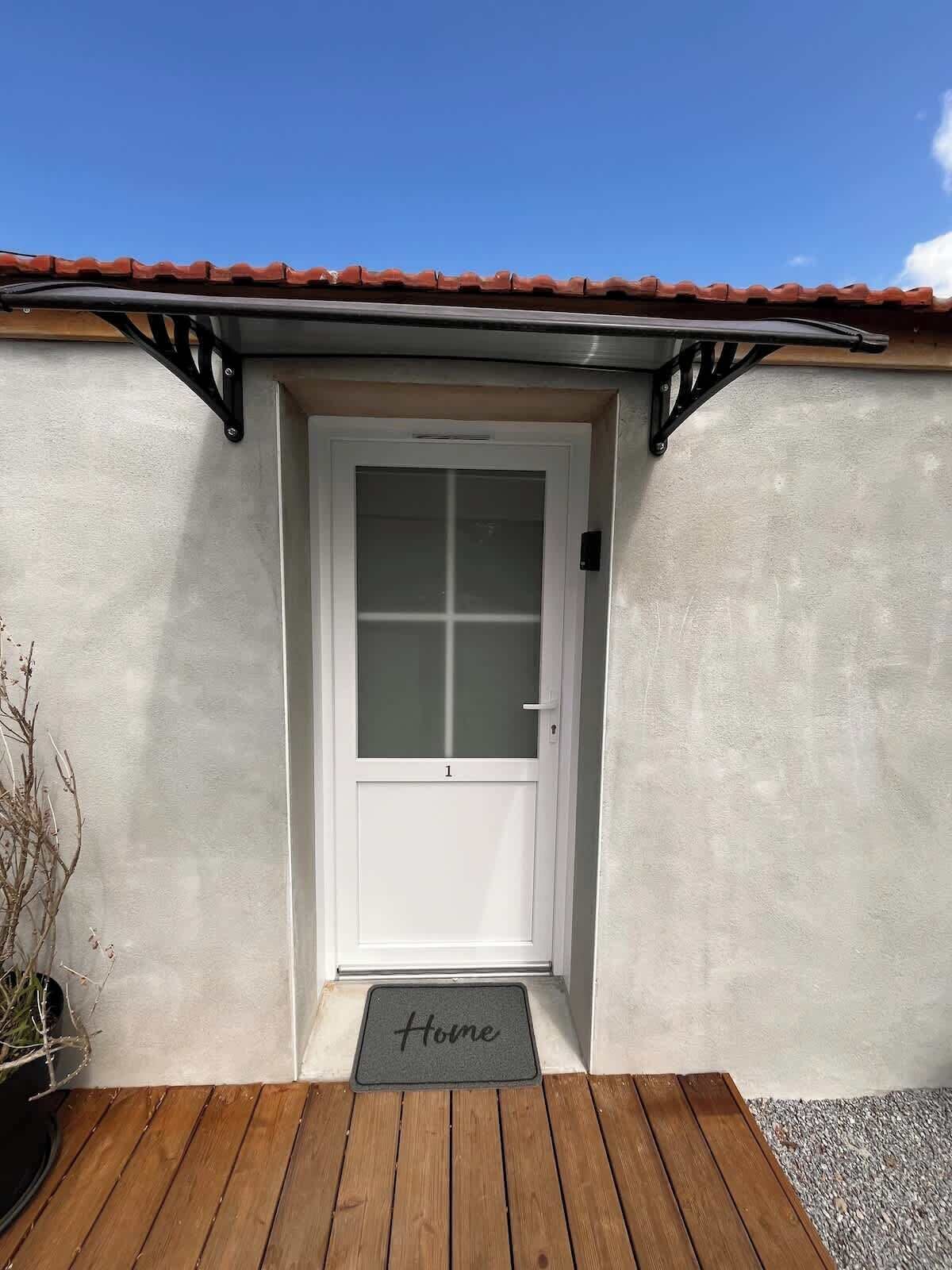 A white door with a frosted glass panel, a small doorbell, and a 'Home' mat at the entrance.