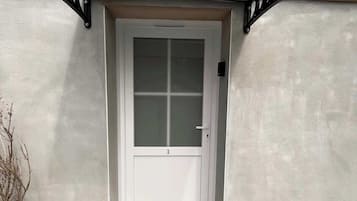 A white door with a frosted glass panel, a small doorbell, and a 'Home' mat at the entrance.
