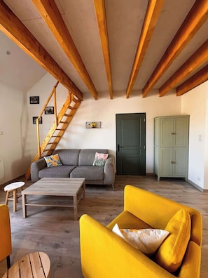 A living room with a staircase, a sofa, a yellow armchair, a wooden coffee table, and a green cabinet.