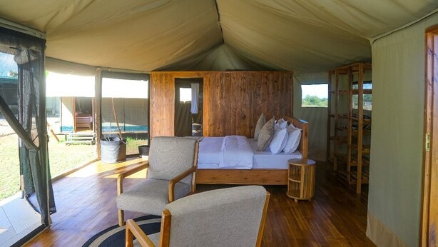 A tented accommodation with a wooden bed, two chairs, and a small table.
