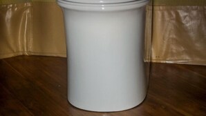 A white toilet with a lid and tank, placed on a wooden floor against a beige wall.