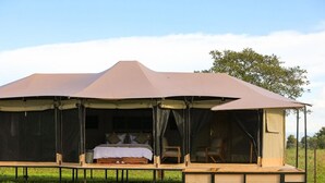 A safari tent with a bed, seating area, and a small table.