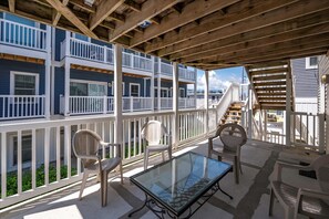 Un espace extérieur abrité, doté d’une table et de chaises en verre, de rampes en bois et offrant une vue sur un immeuble bleu avec des balcons.