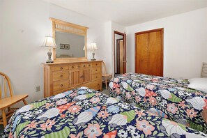 Une chambre avec deux lits, une commode en bois, un miroir et une porte.