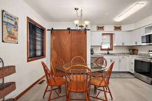 Une cuisine moderne avec des meubles blancs, un four en acier inoxydable et un coin repas comprenant des chaises en bois et une table en verre.