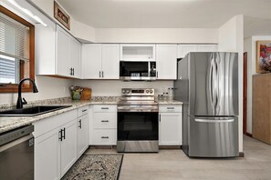 Eine moderne Küche mit weißen Schränken, Edelstahlgeräten, einer Arbeitsplatte aus Granit und einem eingebauten Backofen.
