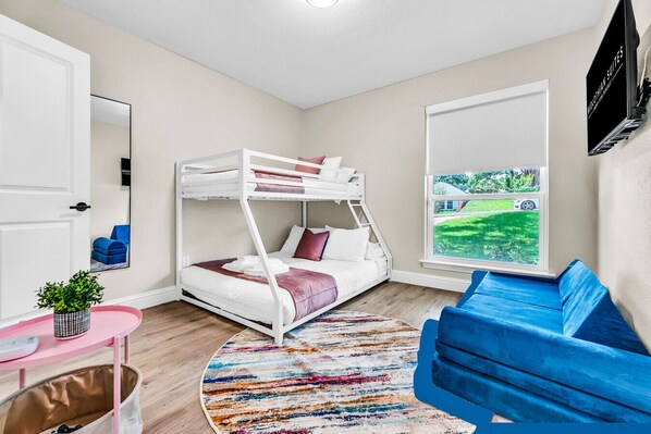 Une chambre avec un lit superposé donnant sur un paysage verdoyant, une chaise bleue et une petite table avec une plante.