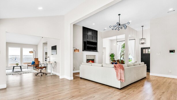A spacious living room with a large white sofa, a fireplace, and a television mounted on the wall. - Newly Renovated, Spacious & Modern | THE (Rockwall)