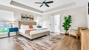 A modern bedroom with a large bed, a ceiling fan, a stone wall, and a view of the outdoors. - Newly Renovated, Spacious & Modern | THE (Rockwall)
