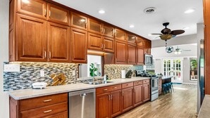 A modern kitchen with wooden cabinets, a stainless steel dishwasher, and a large island with bar stools. - Double Unit, Fenced Yard, Mins to Dal | TMD (Irving)