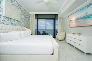 A bedroom with a large bed, a white dresser, a chair, and a painting of a sunset.