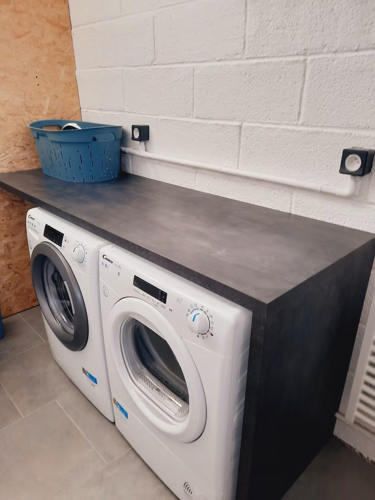 A front-loading washing machine and dryer in a laundry room with a dark countertop and a blue basket on top.