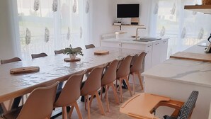 Una cocina moderna con zona de comedor, que incluye una mesa grande, sillas, un televisor y una planta.