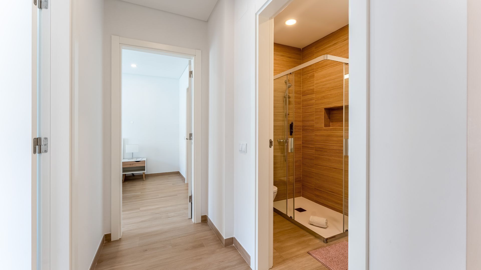 Un bany modern amb una paret de fusta, una cabina de dutxa de vidre i un sòl de fusta.