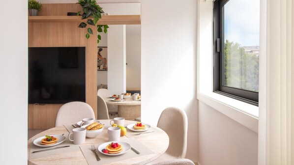 Un coin repas moderne avec une table ronde mise pour le petit-déjeuner, où l’on peut admirer des assiettes de crêpes et des fruits frais.