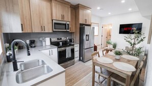A modern kitchen with wooden cabinets, stainless steel appliances, a sink, and a dining area with a table and chairs. - GarageSuite| 2BD + Ping Pong Fun (Edmonton)