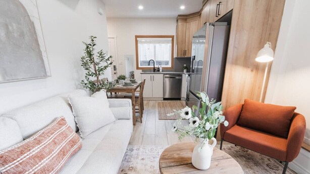 A modern living room with a sofa, a coffee table with a vase, a dining area with a table and chairs, and a kitchen with a refrigerator and stove. - GarageSuite| 2BD + Ping Pong Fun (Edmonton)