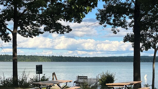 Un espace de pique-nique au bord du lac, équipé de deux tables de pique-nique et d’un panneau d’avertissement.