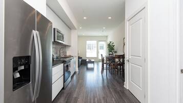 A modern kitchen with stainless steel appliances, a dining area with a table and chairs, and a hallway leading to a door.