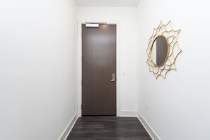 A hallway with a dark wooden door, a white wall, and a gold-framed mirror.