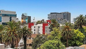 A cityscape with modern buildings, palm trees, and a clear sky. - 2BR Hollywood Apt w/ Rooftop deck & Stunning Views (Los Angeles)