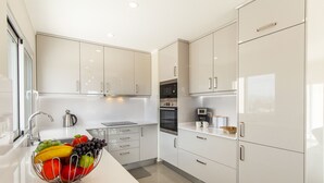 A modern kitchen with white cabinets, stainless steel appliances, and a fruit bowl on the counter. - Villa Oasis Gold (Portimão)