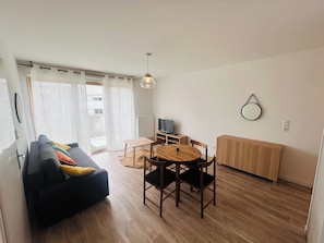 A living room with a sofa, dining table, chairs, a TV, and a radiator. - L'échapée champenoise | Terrasse (Reims)