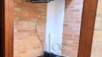 Un armario de madera con una barra para colgar y un objeto vertical blanco, posiblemente una toalla o un cartel, frente a una pared de ladrillo.