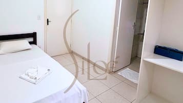 A hotel room with a bed, a door, a shower area, and a shelf.